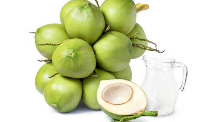 Glass jug of coconut water and young green coconut fruit cluster isolated on white background.